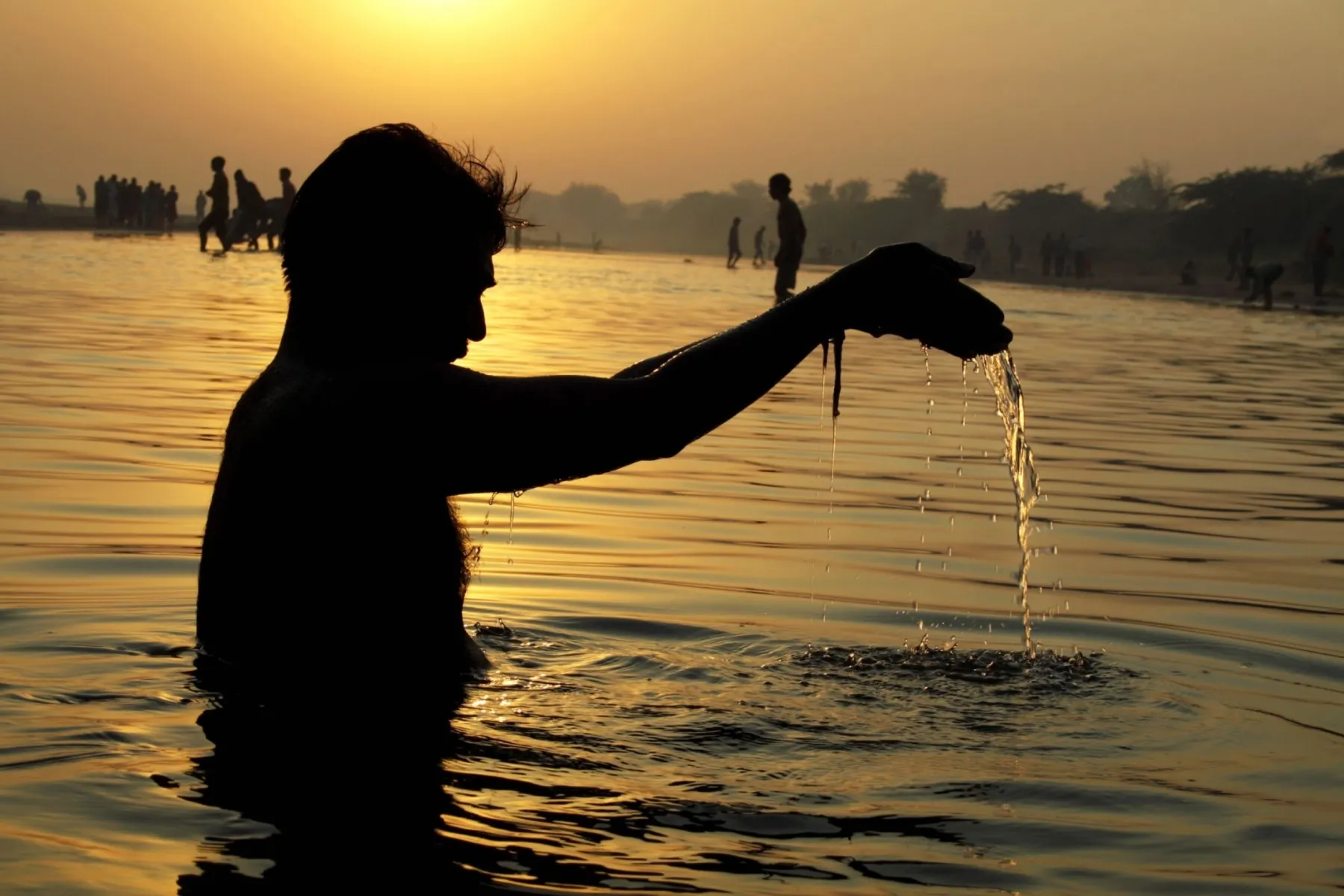 A person offering water at sunset during an ancestral remembrance rite
