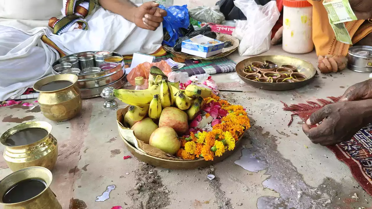 Pictures of  Offerings fruit, flowers, brass pots, and clay lamps are arranged on the ground for a Hindu religious ceremony or puja.