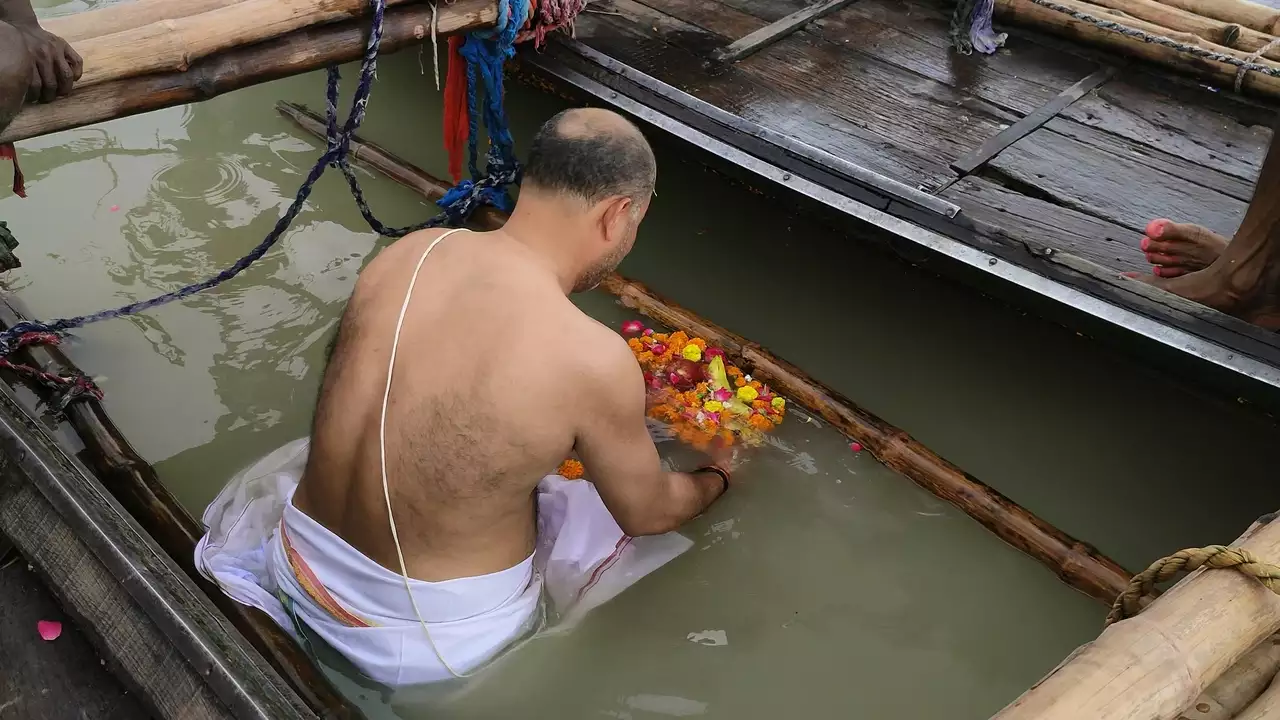 image of Man performs shradh, offering fruits and flowers into the holy river from a boat