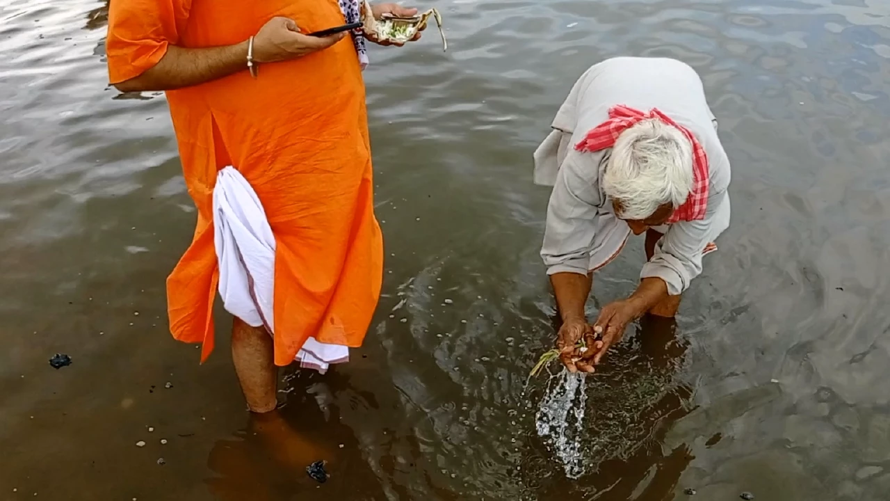 Image of Tarpan ritual in river: Elderly man offers water from hands. Another man stands nearby observing- How many times offer water Tarpan