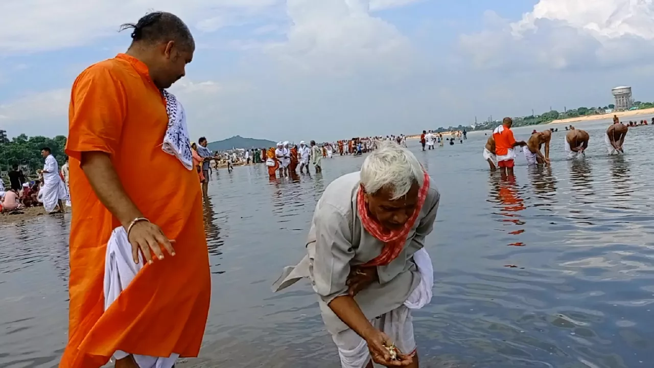 Image of Tarpan ritual in river: Elderly man offers water from hands. Another man stands nearby observing- Sacred Locations for Tarpan