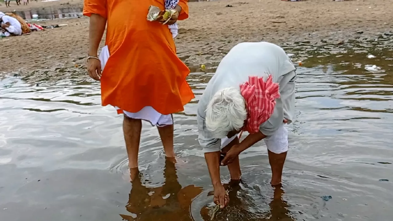 Elderly man performs Tarpan in river, offering water & grass from hands. Another man stands nearby- Tarpan Dos and Donts