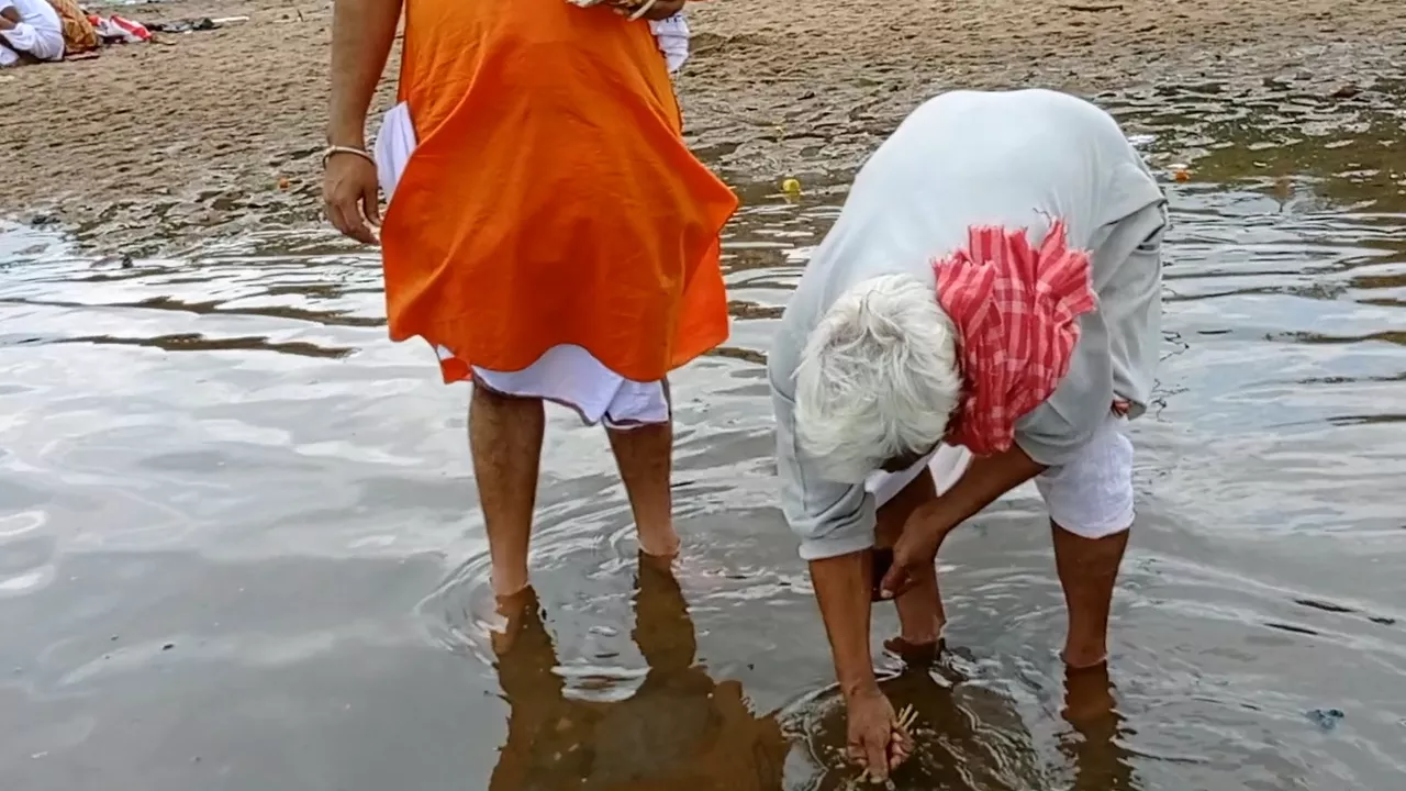 Image of Two men in river. Elderly man performs Tarpan/Shradh ritual, offering water. Other holds items- Tarpan role in Shradh