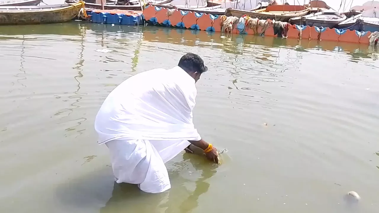 Man in white Dhoti performing Tarpan/Shradh, offering flowers/items in the river for ancestors- Tarpan hand posture mudra

