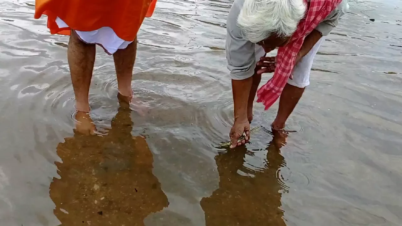 Image of Tarpan ritual in river: Elderly man offers water from hands. Another man stands nearby observing- Sacred Locations for Tarpan