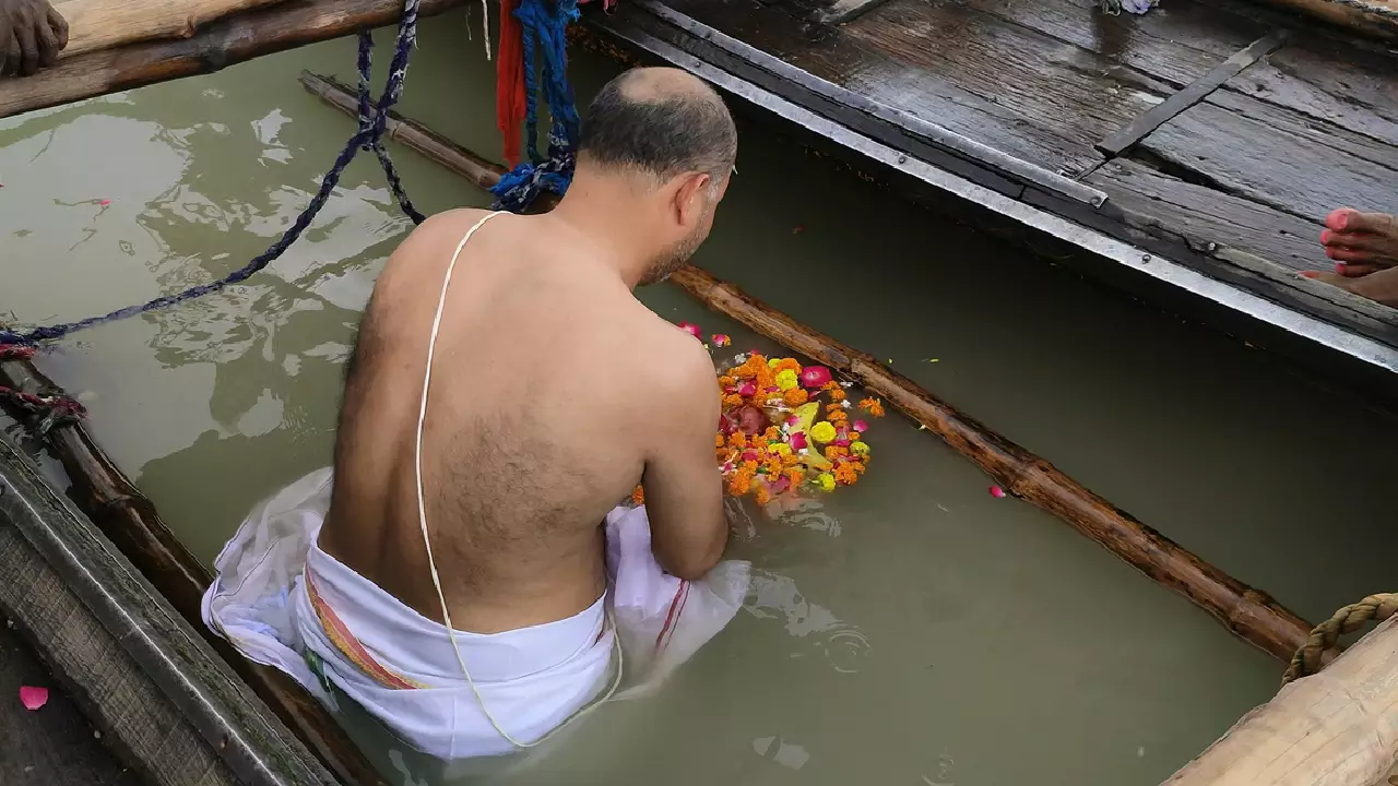 Images of Man performs Tarpan, offering flowers & fruits into the holy river from a boat- Purpose of Tarpan