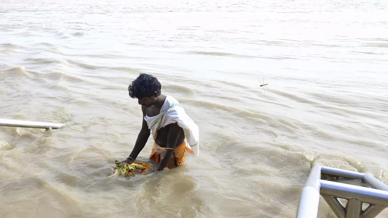 Image of Man performs Tarpan ritual in a river, offering fruits and flowers to ancestors- How to perform Pitru Tarpan