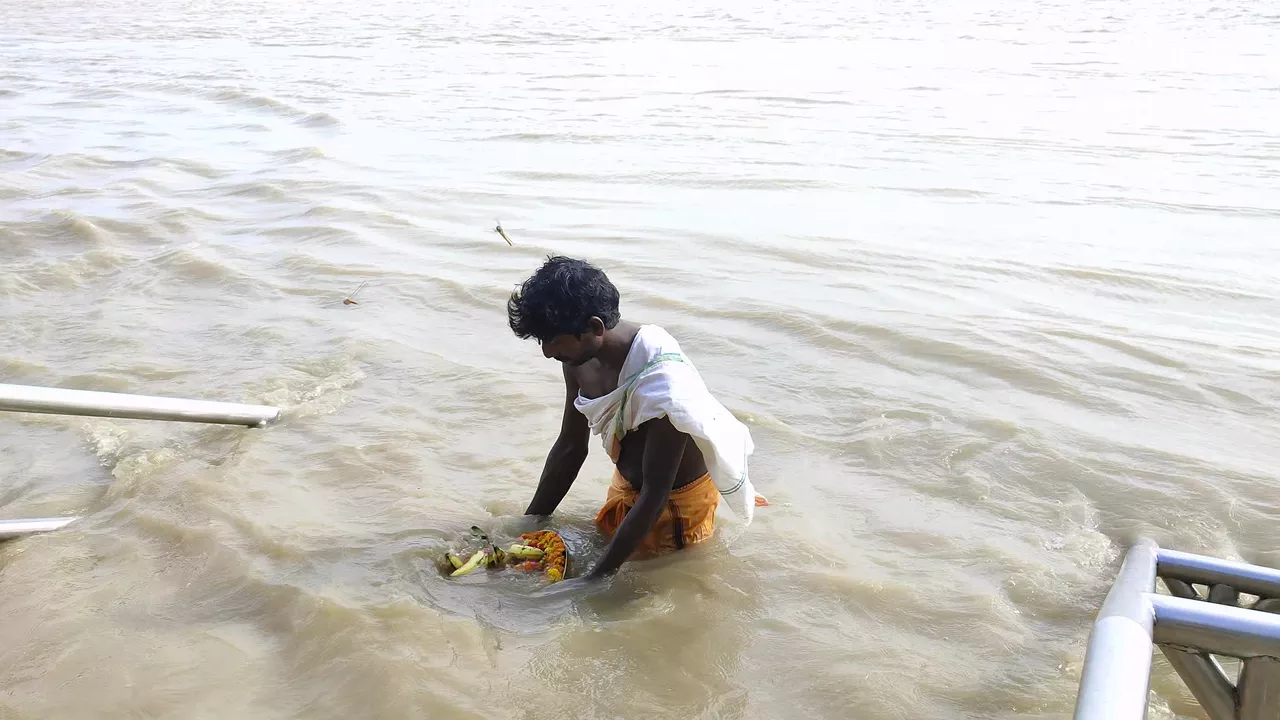 Man performing tarpan ritual in river, offering bananas & flowers on plate. Pitru Paksha observance-Simple Tarpan mantras