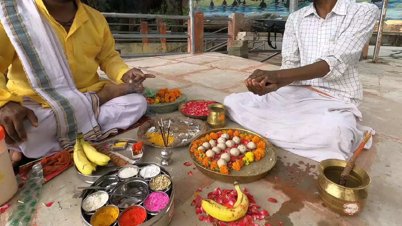 Image of Two men sit facing each other for Shradh ritual. Offerings include Pindas, flowers, altar, fruit- Number of Pindas offered