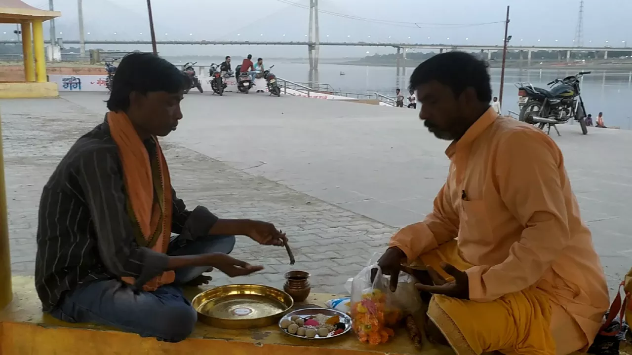 Image of Shradh puja on river bank: two men sit with ritual items, Pindas. River & bridge visible- Pind Daan ritual steps